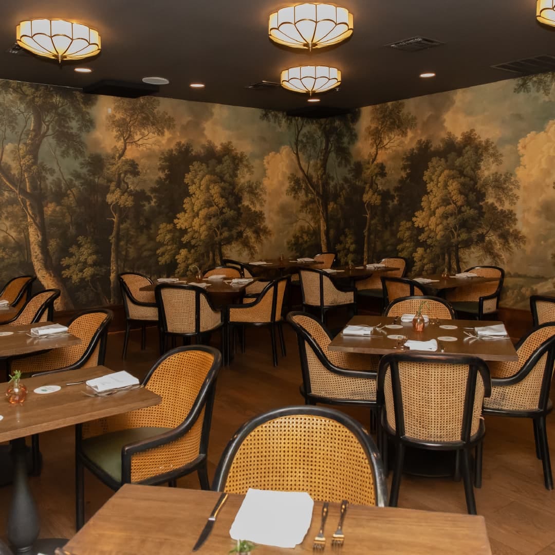 Private Dining Room at The Grove Kitchen & Gardens in Tyler, Texas with warm lighting, wood tables, cane-back chairs, and garden-inspired walls